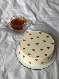 a white cake with red hearts on it next to a cup of tea