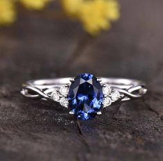 a blue sapphire and diamond ring sitting on top of a piece of wood with yellow flowers in the background