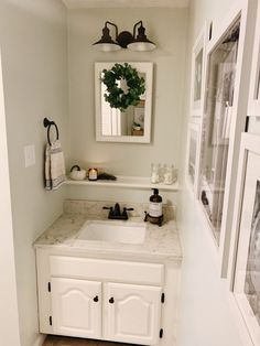 a white sink sitting under a mirror in a bathroom next to a doorway with pictures on the wall