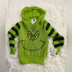 a child's green sweater with an angry grin face on the front and yellow eyes