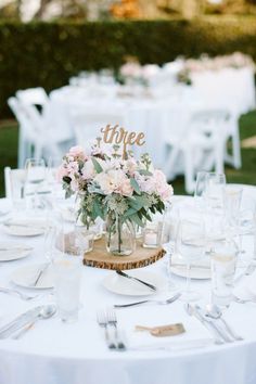 the table is set with white linens, silverware and flowers in vases