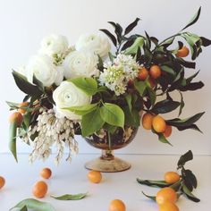 an arrangement of white flowers and oranges in a vase with leaves on the floor