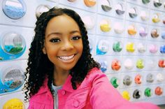 a woman with curly hair smiling in front of a wall full of magnets