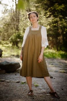 a woman standing in the woods wearing a brown dress and white shirt with her hands on her hips