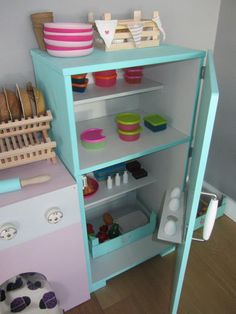 a blue shelf with bowls, plates and other items on it in a play room