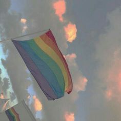 a rainbow flag flying in the sky with clouds behind it and a building on the other side