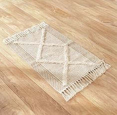 a white rug with fringes on top of a wooden floor in an empty room