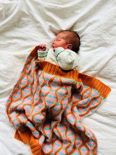 a baby wrapped up in a blanket on top of a white sheet with an orange and blue pattern