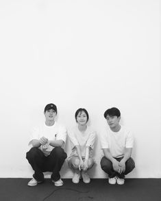 three people sitting on the ground in front of a white wall with black and white background