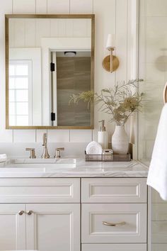 a white bathroom with two sinks and a mirror on the wall above it is decorated with greenery