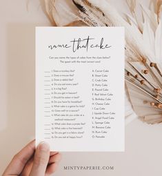 a hand holding up a printable name that cake game next to feathers and flowers