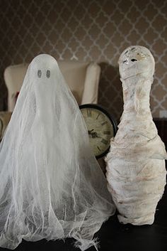 two stuffed animals dressed as ghostes on a table next to a clock and chair