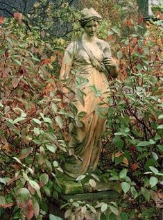 a statue in the middle of some bushes and trees with red leaves on it's sides