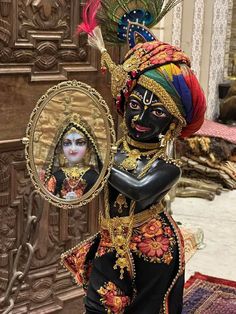 a woman dressed in black and gold holding a mirror with her face painted on it