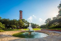 a water fountain in the middle of a park with a clock tower in the background