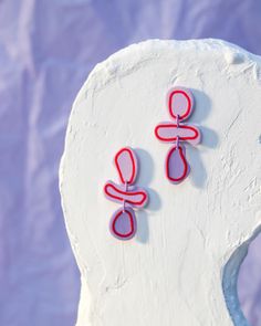 two red and pink earrings sitting on top of a white sculpture