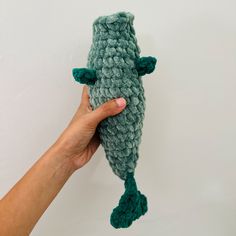 a hand holding a green crocheted stuffed animal in the shape of a fish