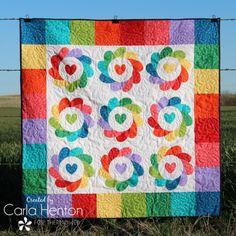 a multicolored quilt hanging on a wire fence in the middle of a field