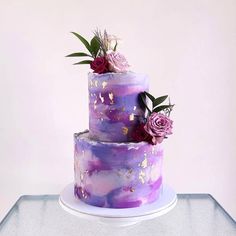 a three tiered cake with purple and pink flowers on top is sitting on a white plate