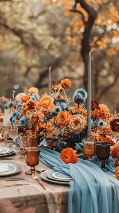 the table is set with blue and orange flowers, candles, and napkins on it