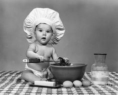 a baby in a chef's hat sitting on a table with food and utensils