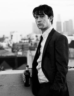 a man in a suit and tie holding a beer bottle while standing on a balcony