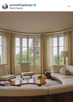 a living room with two chairs and a table in front of large windows that look out onto the eiffel tower