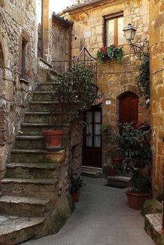 an alleyway with oranges and potted plants on the steps leading up to a door