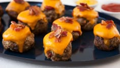 mini hamburgers with cheese and bacon are on a black plate, ready to be eaten