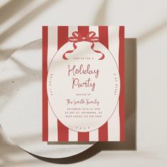 a red and white striped holiday party card with a bow on the front, sitting on top of a plate