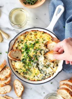 a person dipping some bread into a casserole with spinach and cheese on it