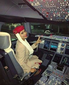 a woman sitting in the cockpit of an airplane pointing at the buttons on the control panel