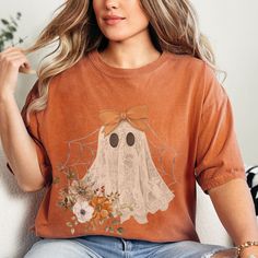 a woman sitting on a couch wearing an orange shirt with a ghost drawn on it