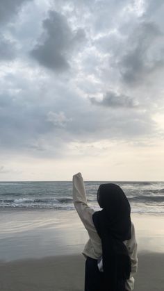 a woman standing on top of a beach next to the ocean under a cloudy sky