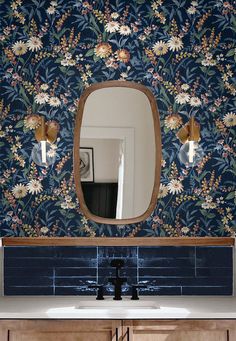 a bathroom sink under a large mirror next to a wall mounted vanity with flowers on it