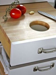 two tomatoes and a knife on a cutting board next to an open drawer with drawers