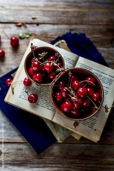 two bowls filled with cherries on top of an open book