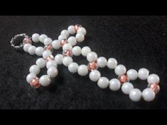 a cross made out of white beads on a black surface with an orange bead cord