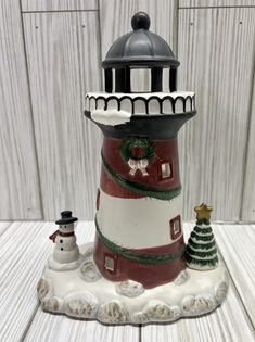 a ceramic lighthouse with a christmas tree on it's top and snowmen standing next to it