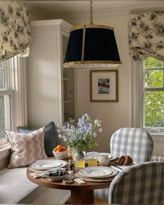 a dining room table set for two with plates and cups on it, next to a window