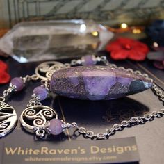 a purple stone is sitting on a table next to some silver chains and pendants