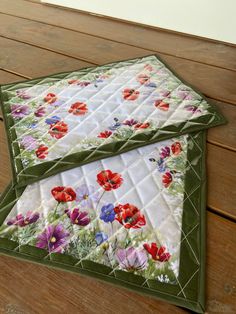 two quilted placemats sitting on top of a wooden table next to each other