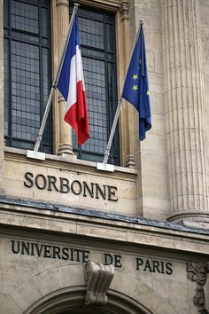 two flags are flying in front of the entrance to a building with columns and windows