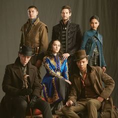 a group of people sitting next to each other in front of a black background with one man wearing a top hat