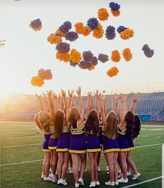 a group of cheerleaders standing on top of a field with their hands in the air