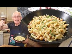 an old man holding a bowl of pasta and a glass of wine in front of him