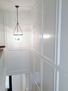 a hallway with white walls and a light fixture hanging from it's ceiling above the stairs