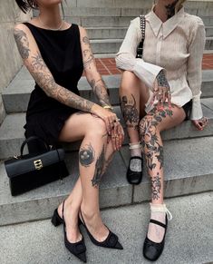 two women sitting on the steps with tattoos on their arms and legs, both holding purses