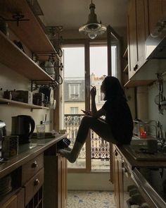 a woman sitting on top of a counter in a kitchen next to an open window