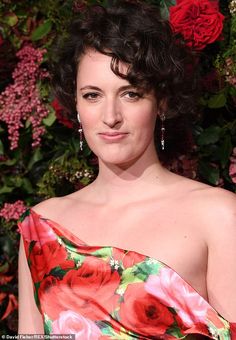 a woman in a floral dress posing for the camera with flowers on her wall behind her